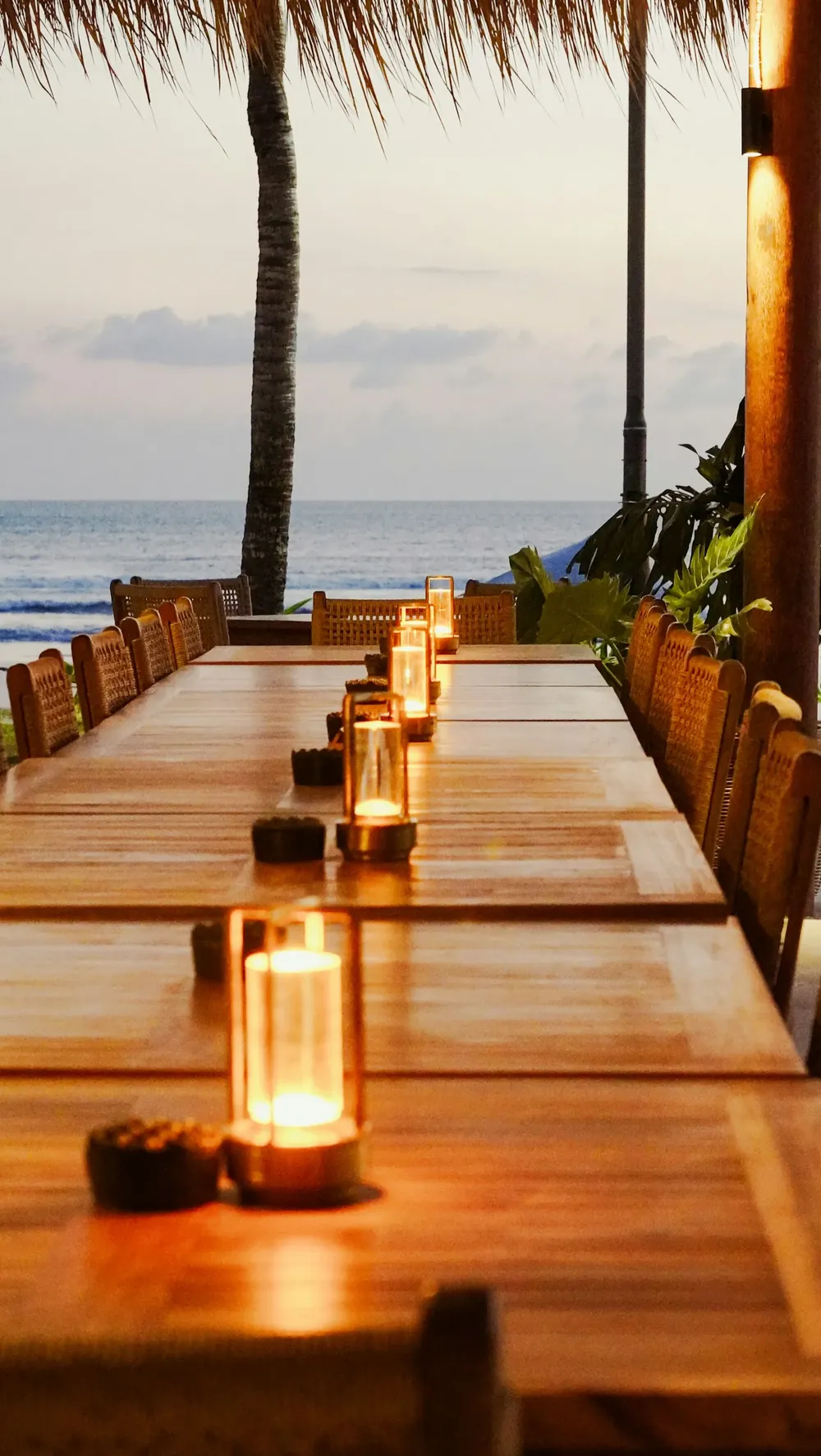 A long candlelit table set beside the sea under palm trees