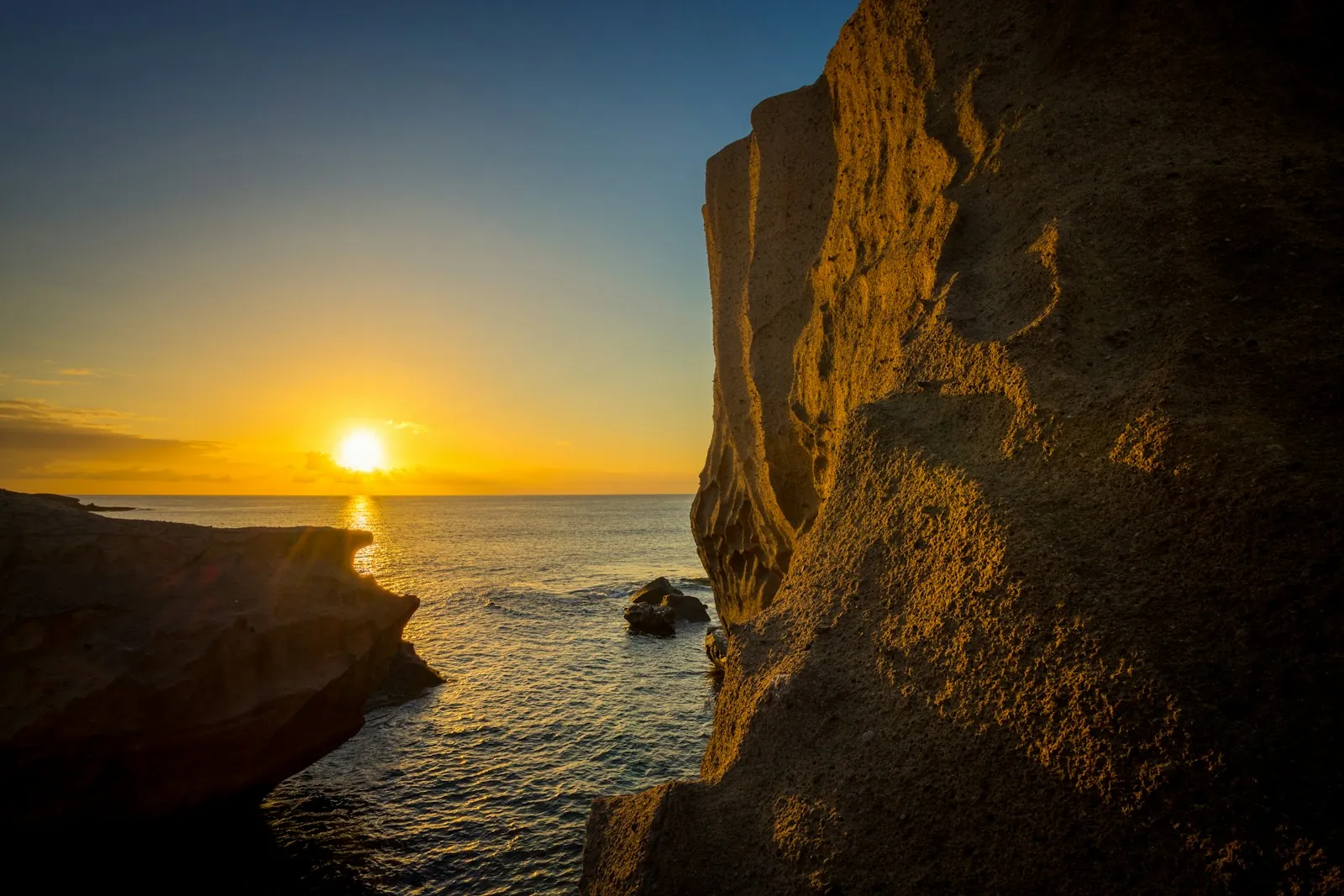 The sun setting over the sea beside a volcanic cliff